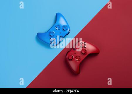 Zwei xbox Gamepads liegen einander auf blauem und rotem Hintergrund gegenüber Stockfoto