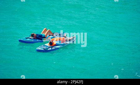 Mann und Frau liegen auf einem Stand-Up-Paddle-Brett. Ein Paar, das sich Zeit nimmt, sich auf einem Tisch zu entspannen. Sommer Outdoor Aktivitäten am Meer. Familie RE Stockfoto