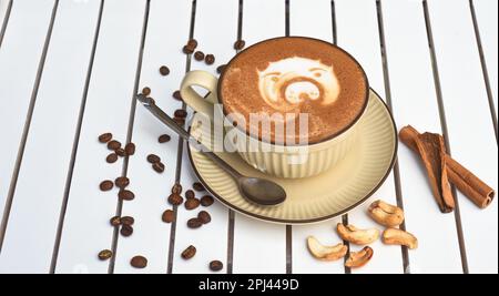 Eine Tasse Nuss-Cappuccino mit Löffel und Zucker auf einem weißen Holztisch mit seitlichem Blick Stockfoto