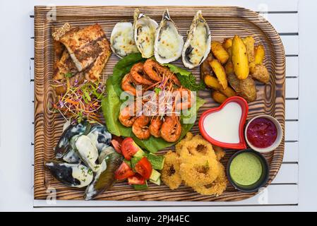 Viele Meeresfrüchte wie gebratener Fisch, Calamari, Austern und Soßen auf dem Holzbrett auf dem Tisch Stockfoto