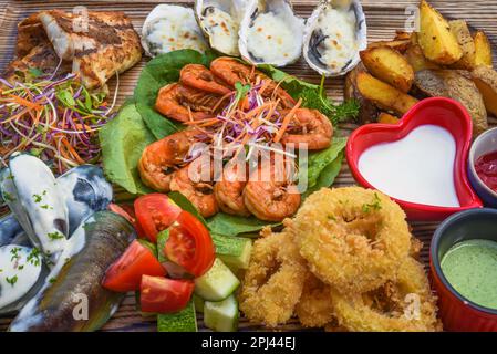Viele Meeresfrüchte wie gebratener Fisch, Calamari, Austern und Soßen auf dem Holzbrett auf dem Tisch Stockfoto