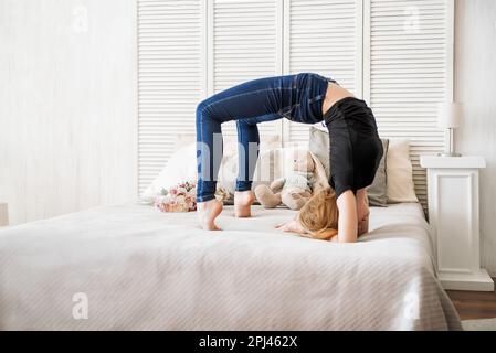 Ein junges Mädchen, das Gymnastik auf weißem Hintergrund macht, ein Mädchen, das eine Turnerbrücke macht, auf dem Bett, im Zimmer Stockfoto