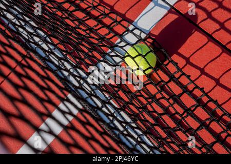 Selektiver Fokus, ein Ball im Netz eines Tennisplatzes, rot gestrichen Stockfoto