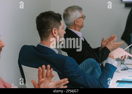 Nahaufnahme von drei Geschäftsleuten, die am Büroschreibtisch sitzen, während sie der Präsentation zuhören Stockfoto