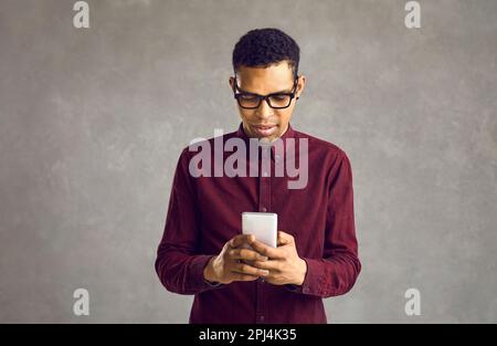 Junger afroamerikanischer Mann, der Textnachrichten sendet oder mobile Apps auf seinem Smartphone verwendet Stockfoto