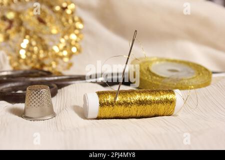 Rolle mit goldmetallischem Gewinde und Schere mit Kaugummi auf weißem Stoff mit goldfarbenen Pailletten Stockfoto