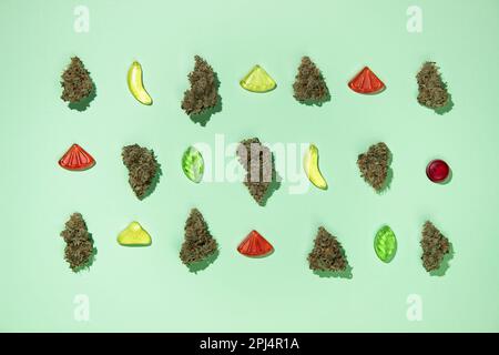Trockene Knospen von medizinischem Marihuana liegen in Ordnung vermischt mit kauigen Süßigkeiten auf einem Minzhintergrund. Draufsicht, Platz sparen, Gummibonbons Stockfoto