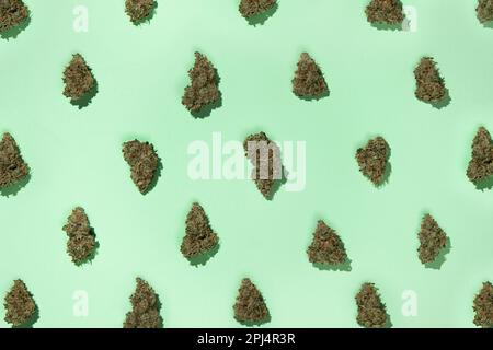 Ein Muster von trockenen Knospen medizinischen Marihuanas, angeordnet in einem Schachbrettmuster, auf einem Minzhintergrund. Stockfoto