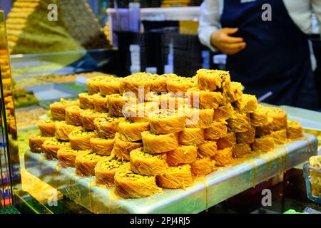 Stapel Baklava im Vordergrund und die Hände eines unbekannten Verkäufers bedienen die Gäste im traditionellen türkischen Delights Shop. Eine Schachtel türkischer Konfetti Stockfoto
