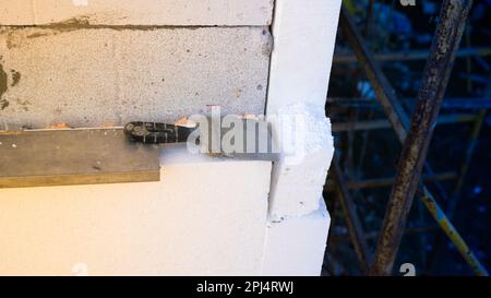 Ein alter Spachtel liegt auf dem Schaumstoff, der an der Wand des Hauses befestigt ist. Isolierung eines Hauses mit Wänden aus Porenbetonsteinen mit Polystyrolschaum Stockfoto