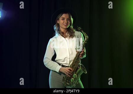 Schöne junge Frau mit Saxophon auf dunklem Hintergrund Stockfoto