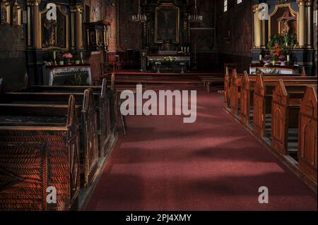 Blick nach Osten in Richtung des Altars einer 1700er Jahre alten Dorfkirche, die teilweise wiederaufgebaut und vollständig restauriert wurde, nachdem sie bei einem Brandanschlag von 1994 von einem Feuer verwüstet wurde. Die 1757 erbaute barocke hölzerne Kirche des Heiligen Kreuzes in Rdzawka im Bezirk Nowy Targ im Süden Polens verfügt jetzt über Bergungsbänke und Armaturen auf der nördlichen (linken) Seite und nur noch moderne Armaturen im südlichen Marineschiff auf der rechten Seite. Stockfoto