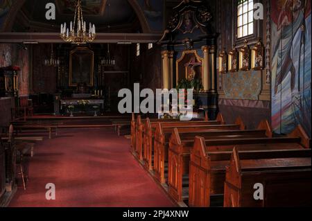 Südöstlich in Richtung Altar der polnischen Dorfkirche, die nach einem Brandanschlag von 1994 durch einen Brand wiederhergestellt wurde. Das wiederaufgebaute Südschiff der barocken hölzernen Kirche des Heiligen Kreuzes in Rdzawka in Nowy Targ County, Südpolen, gegründet 1757, verfügt jetzt über moderne Bänke und Armaturen, mit geborgenen Bänken und geretteten Kunstwerken entlang des gegenüberliegenden Nordschiffes. Stockfoto