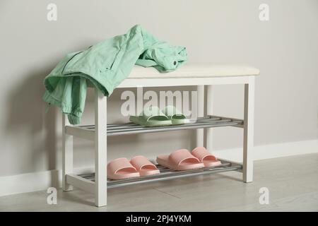 Elegante Aufbewahrungsbank mit verschiedenen Paar Gummipantoffeln an der weißen Wand im Flur Stockfoto