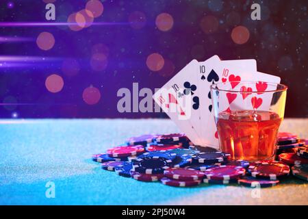 Alkoholgetränk, Spielkarten und Casino-Chips auf dem Tisch gegen verschwommene Lichter, Platz für Text. Eine vierfache Pokerkombination Stockfoto