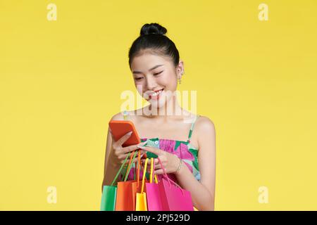 Glückliche junge asiatische Frau feiert mit Handy und Einkaufstaschen in der Hand Stockfoto