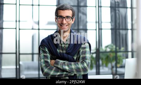 Aufnahme eines hübschen jungen Geschäftsmannes, der allein in seinem Büro mit gefalteten Armen stand. Stockfoto