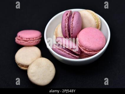 Makronen auf einer weißen Platte auf schwarzem Hintergrund. Makronen in einer Keramikschüssel. Bunte süße Kekse. Stockfoto