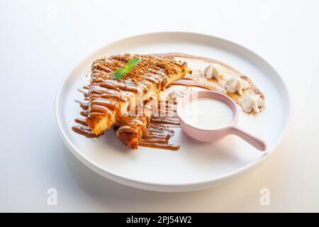 Französischer Toast in Lotusknusprig-Keksgeschmack, serviert auf einem weißen Teller mit Sahne-Sauce. Stockfoto
