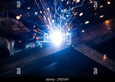 Nahaufnahme der Metallbearbeitung in einer dunklen Werkstatt. Schweißen und Schleifen mit viel Funken und Rauch Stockfoto