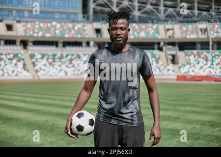 Ein junger Mann steht in einem Stadion mit einem Fußball in der Hand Stockfoto