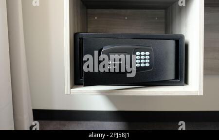 Metallsafe im Schrank. Kleiner, schmaler Safe, in dem man Geld oder Wertsachen im Hotel aufbewahren kann. Öffnen Sie die sichere Tür mit Tasten zur Passworteingabe. Stockfoto