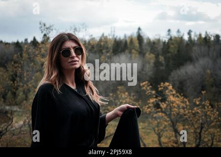 Porträt einer jungen Frau mit Sonnenbrille, während sie gegen den Baum steht Stockfoto