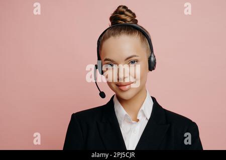 Angenehm aussehende Büroangestellte in dunklem Anzug mit schwarzem, schnurlosem Headset, die über eine Webkonferenz mit Kollegen kommunizieren und sich mit ihnen unterhalten Stockfoto