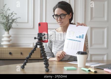 Technologie und Blogging-Konzept. Positive Couch-Lady, die zu Hause Videoinhalte für ihren Blog aufzeichnet, Online-Podcast auf dem Handy auf dem Stativ streamt Stockfoto