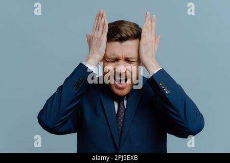 Unternehmerisches Scheitern. Unzufriedener, frustrierter Geschäftsmann oder männlicher Unternehmer in Anzügen, der Kopf in den Händen hält und laut schreit, weil er schlechte Negate erhält Stockfoto