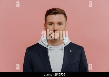 Porträt eines gutaussehenden, selbstbewussten jungen Mannes, der ein elegantes, legeres Outfit trägt, in die Kamera schaut, in guter Stimmung ist, während er isoliert über Staub steht Stockfoto