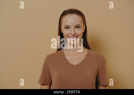 Natürliche Schönheit. Junge, charmante Frau mit gesunder Haut und gesundem Haar, die vor der Kamera lächelt, attraktive Frau mit täglichem Make-up, die ein einfaches beiges T-Shirt trägt, de Stockfoto