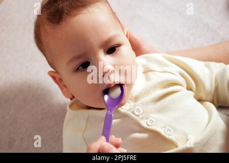 Trinkwasser oder Arzneimittel Hustensaft mit Löffel, Nahaufnahme. Kleines Baby trinkt medizinischen Sirup. Stockfoto