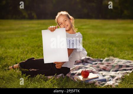 Teenager-Schülerin mit Poster oder Plakat in den Händen, die nach dem Unterricht im grünen Park sitzt Stockfoto