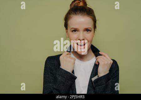 Porträt einer jungen, überfreulichen, trendigen Frau in legerer Kleidung, die einen Jackenkragen hält und mit aufgeregtem Gesichtsausdruck, Einstellung in die Kamera schaut Stockfoto