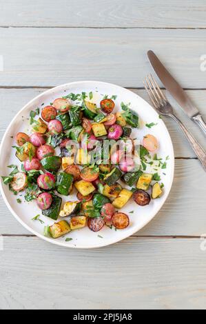 Marinierter Gemüsesalat mit geröstetem Rettich und Zucchini. Serviert warm mit gehackter Petersilie auf einem Teller, isoliert auf hellem Holzhintergrund Stockfoto