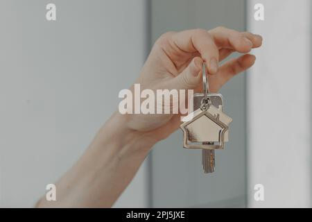 Hypothekendarlehen. Weibliche Hand-Hand-Schlüsselanhänger in Hausform, verkürztes Bild einer Frau, die Schlüssel aus der neuen Wohnung zeigt, Immobilien kauft und eine verlegt Stockfoto