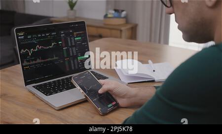 Junge Finanzanalytiker kaufen und verkaufen Krypto auf dem Aktienmarkt mit Laptop und Smartphone Stockfoto