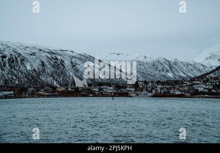 Eine atemberaubende Winterszene an einer ruhigen Küste in Tromso, Norwegen, mit malerischen schneebedeckten Bergen im Hintergrund Stockfoto