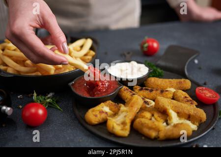 Frau taucht pommes in Dip-Sauce mit gebratenen Mozzarella-Stäbchen auf einem Tisch Stockfoto