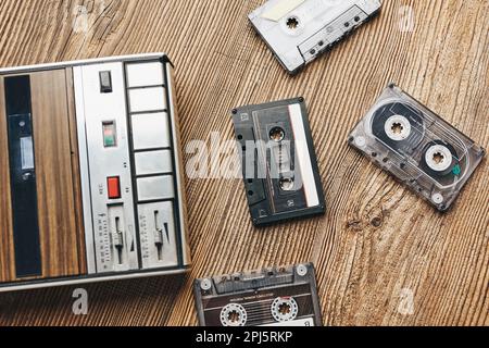 Kompakte Kassettenbänder und Kassettenrekorder auf Holztisch. Retro-Musikstil. 80s Musikparty. Vintage-Style. Analoges Gerät. Stereo-Sound. Zurück Stockfoto