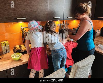 Gruppe von Kindern, die Cupcakes backen, Zutaten zubereiten, Toppings, Streuseln zum Dekorieren von Keksen. Kinder lernen kochen, arbeiten zusammen Stockfoto