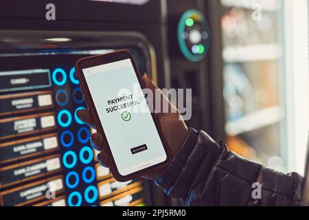 Verbraucher, der für das Produkt am Verkaufsautomaten mit kontaktloser Zahlungsmethode mit dem Mobiltelefon bezahlt. Frau, die die Zahlungs-App auf dem Smartphone verwendet, um Pro zu kaufen Stockfoto