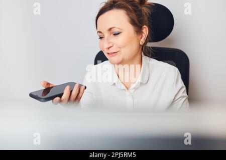 Geschäftsfrau, die im Freisprechmodus auf dem Mobiltelefon spricht. Frau, die mithilfe der Sprachassistenz- und Erkennungsfunktion auf dem Smartphone Audionachrichten aufzeichnet. Stockfoto