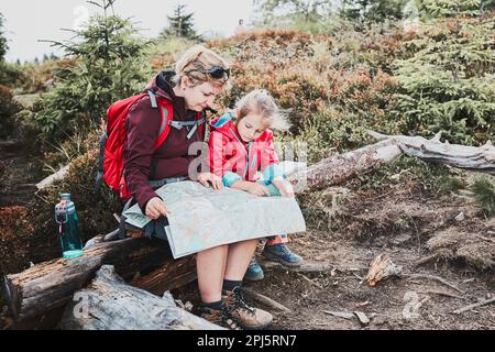 Familienausflug in die Berge. Mutter und ihre kleine Tochter untersuchten eine Karte, saßen auf dem Stumpf, machten während der Sommerreise Pause Stockfoto