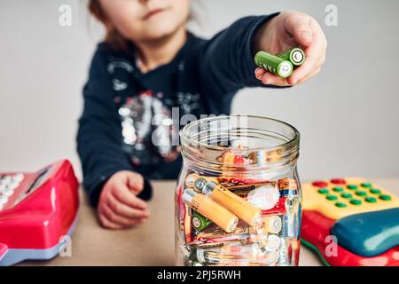 Kleines Mädchen, das gebrauchte Batterien zum Recycling in den Becher legte. Kinder trennen Abfall. Behälter nur für Batterien Stockfoto