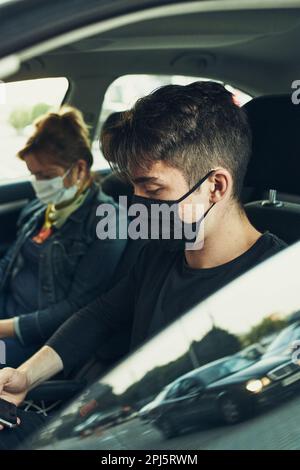 Mann und Frau sitzen in einem Auto mit Smartphones tragen die Gesichtsmasken, um Virusinfektion zu vermeiden und die Ausbreitung der Krankheit in der Zeit von coron zu verhindern Stockfoto
