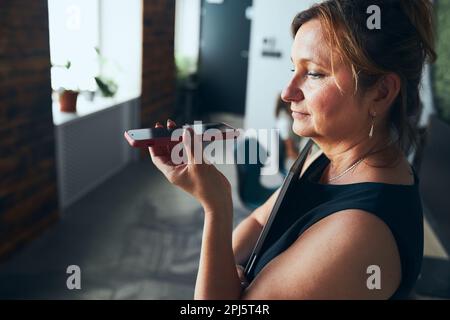 Eine Frau, die geschäftlich im Büro arbeitet. Erwachsene Frau, die mit dem Lautsprechermodus über ein Mobiltelefon spricht. Mit Technologie. Fernkommunikation. Fernsteuerung Stockfoto