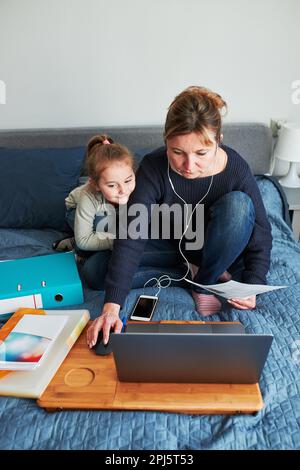Frau, die während eines Videochats per Fernzugriff arbeitet, streamen Sie das Webinar des Online-Kurses von zu Hause aus auf einem Laptop, während ihre Tochter herumspielt Stockfoto
