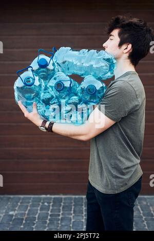 Junger Mann wirft leere, gebrauchte Plastikflaschen in den Abfalleimer. Sammeln von Kunststoffabfällen zum Recycling. Konzept der Plastikverschmutzung und zu ma Stockfoto